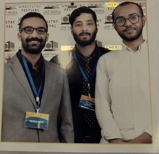 Photograph of three chemistry-festival participants before a Qatar University backdrop